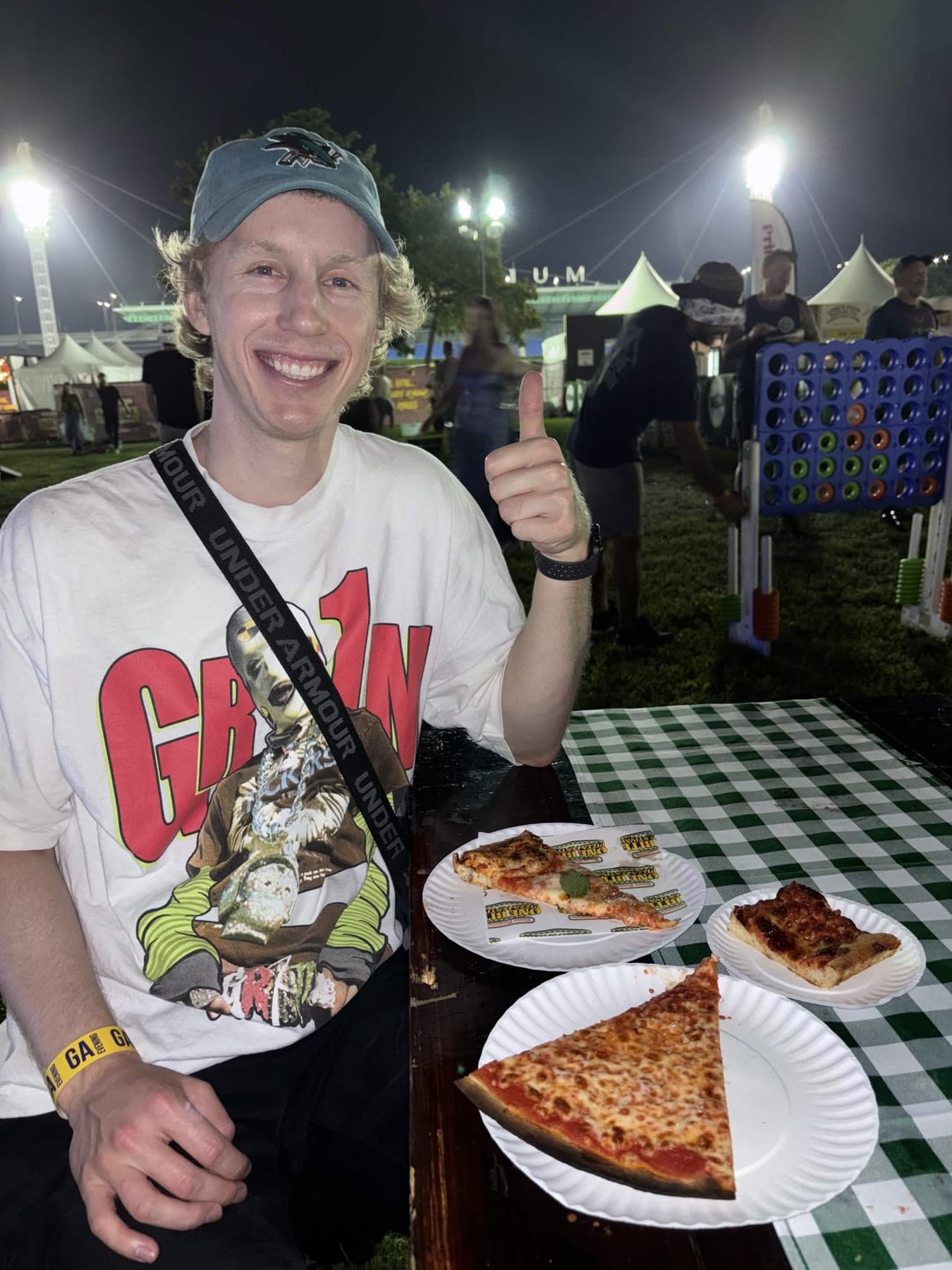 Garrett giving a thumbs up at the pizza festival at night, three slices in front of him.