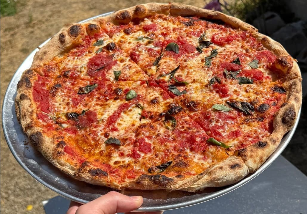A cheese and basil pie, just out of the oven, held up on its tray.