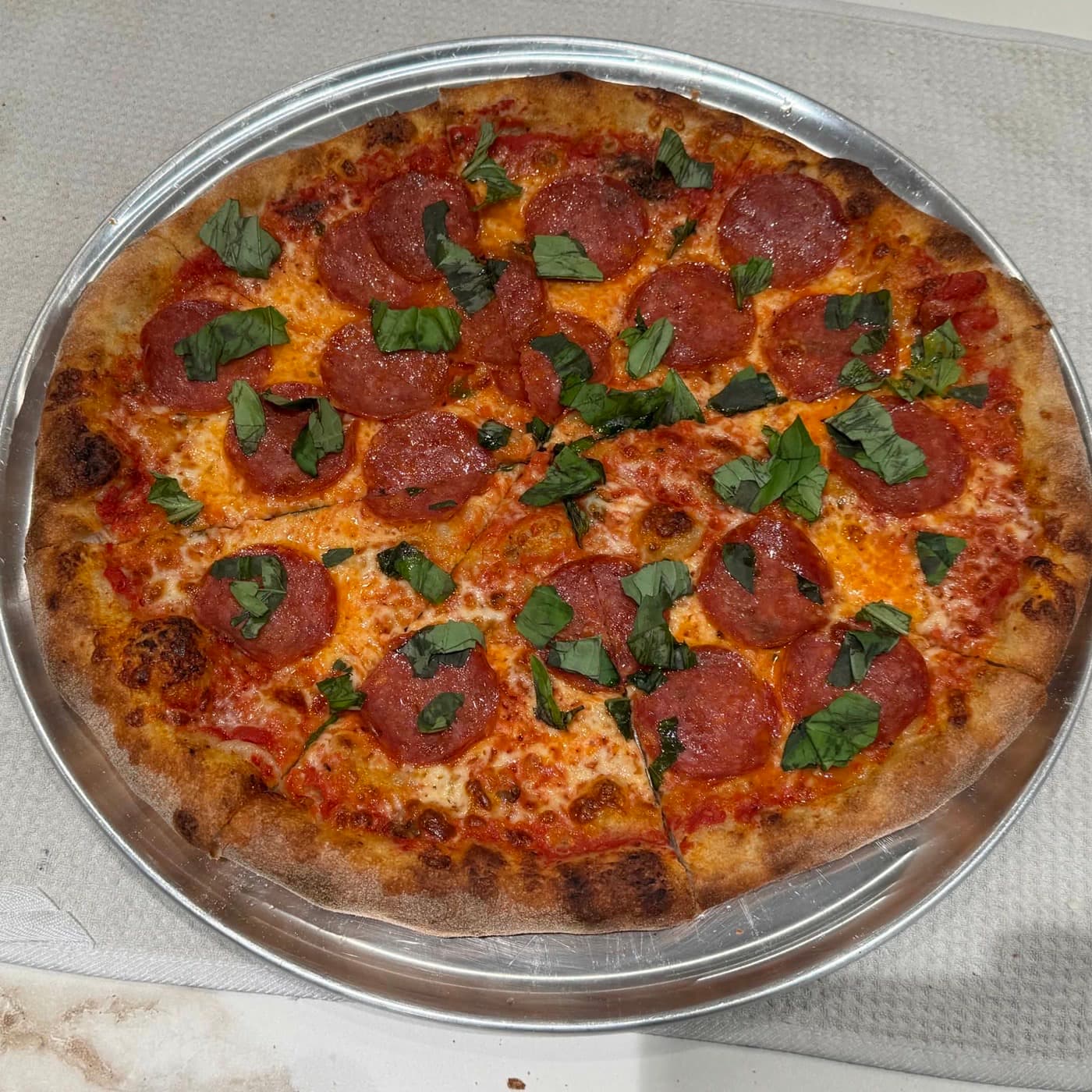 A pepperoni pie with fresh basil on a silver serving tray.